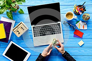 Business person holding dollars by laptop on blue wooden table