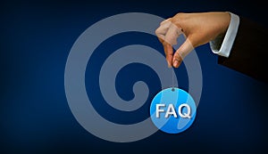 Business person holding FAQ sign on blue background