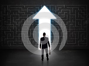 Business person looking at maze with solution arrow on the wall