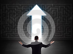 Business person looking at maze with solution arrow on the wall