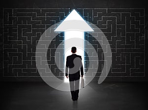 Business person looking at maze with solution arrow on the wall