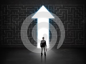 Business person looking at maze with solution arrow on the wall