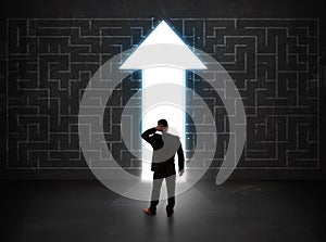 Business person looking at maze with solution arrow on the wall