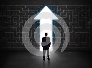 Business person looking at maze with solution arrow on the wall
