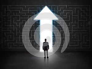 Business person looking at maze with solution arrow on the wall