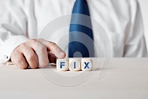Business person pressing his finger on the wooden cubes with the word fix. To find a solution and fixing business dilemmas