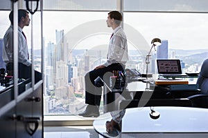 Business Person Sits On Desk Looking Out Of Office Window