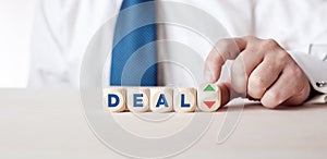 Business person is turning a wooden cube with the arrows next to the word deal. The decision or dilemma to accept or reject a