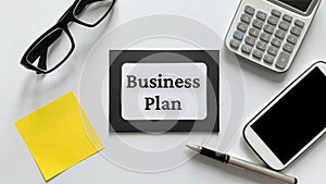 Business plan text on notepad with glasses, calculator, phone and yellow sticky note background. Business concept.