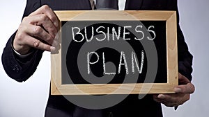 Business plan written on blackboard, male hands holding sign, strategy, goals