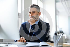 Business planning concept. Thoughtful middle aged businessman sitting at desk with computer, working in office