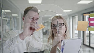 Business planning, man and woman using sticky notes on glass whiteboard brainstorming supervisor woman working with