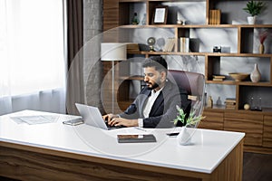 Business portrait, bearded businessman sitting in modern stylish office working with laptop