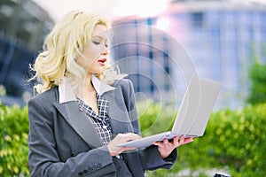 Business portrait of a blonde woman. Office worker working at a laptop outside.