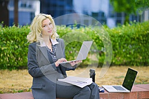 Business portrait of a blonde woman. Office worker working at a laptop outside.