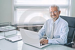 Business portrait of an elderly man. An aged man working on a laptop, looking at the camera and smiling. Work on removal