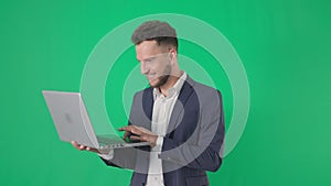 business portrait, smiling businessman straightens his jacket and catches laptop, smiling and looking at camera on green