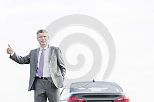 Business professional hitchhiking by breakdown car against sky