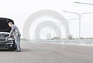 Business professional looking at breakdown car on road against sky