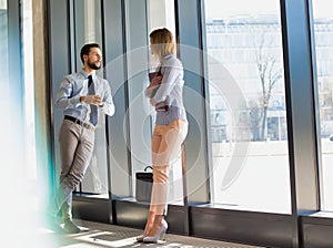 Business professionals discussing plans while leaning on window in office hall