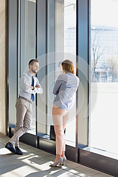 Business professionals talking while leaning on wall in office hall during break