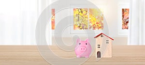 Business property investment model wooden house with piggy bank on bright interior room background with copy space, financial real