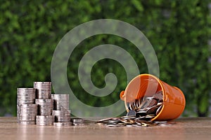 Business property investment stacking coins saving growth with stainless cup filled with coins on wooden desk and green background