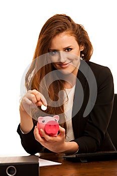 Business savings - woman in the office with piggy bank and coin