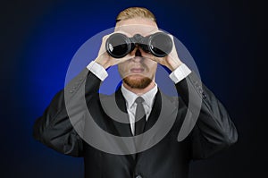 Business and search topic: Man in black suit holding a black binoculars in hand on a dark blue background in studio isolated