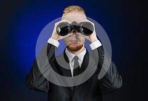 Business and search topic: Man in black suit holding a black binoculars in hand on a dark blue background in studio isolated