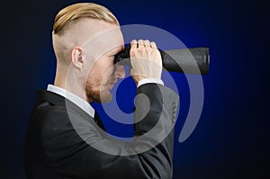 Business and search topic: Man in black suit holding a black binoculars in hand on a dark blue background in studio isolated