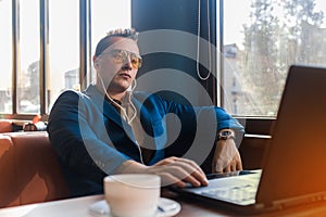 A business serious man businessman a stylish of Caucasian appearance, in sunglasses, works in a laptop or computer, sitting at a