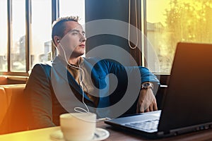 A business serious man businessman a stylish of Caucasian appearance, works in a laptop or computer, sitting at a table by the