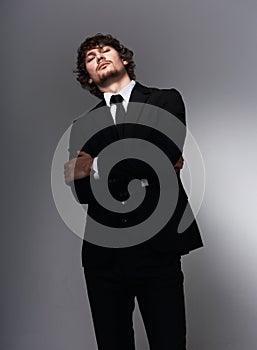 Business sexy man in black fashion suit posing on gray bacground with serious face and passion angry look. Closeup