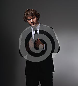 Business sexy man in black fashion suit posing on gray wall background with serious face and passion angry look. Closeup studio