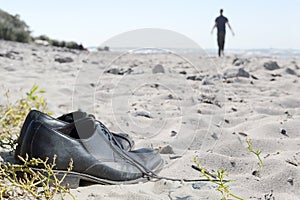 Business shoes at the beach and a blurred man walking away to th