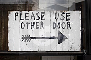 Business sign in black and white with an arrow icon please use other door