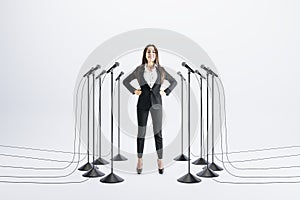 Business speaker concept with confident businesswoman and floor stand microphones around on white background