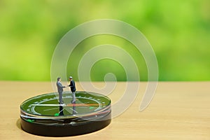 Business strategy conceptual photo - Two miniature businessman make handshake partnership agreement above compass