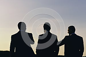 Business and success concept. Silhouettes of men standing against sunset. Leaders discuss project.