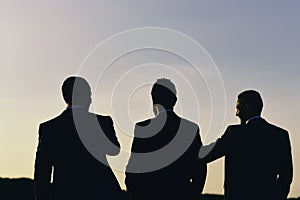 Business and success concept. Silhouettes of men standing against sunset. Leaders discuss project. photo