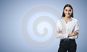 Business success concept with young smiling woman folded her hands in white shirt on abstract light blue background with copyspace