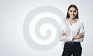 Business success concept with young smiling woman folding her hands in white shirt and black trousers on abstract light blank