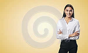 Business success concept with young smiling woman folding her hands in white shirt and black trousers on abstract light orange