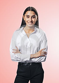 Business success concept with young smiling woman folding her hands in white shirt and black trousers on abstract light pink