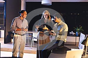Business team collaborating on digital devices in modern office at night