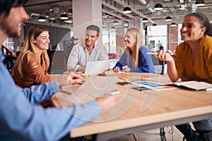 Business Team Having Meeting Sitting Around Table In Modern Open Plan Office