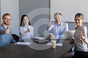 Business team looking at camera showing thumbs up at meeting