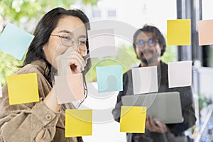 Business team meeting planning new strategy using colored sticky notes on mirror board in workplace