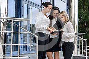 Business team with tablets posing outside office building. Three ladies looking directly on tablet screen